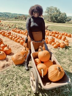 a woman is pushing a wheelbarrow filled with pumpkins in an open field