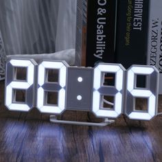 an alarm clock sitting on top of a wooden table next to books and a lamp