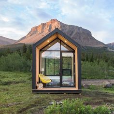 a small cabin in the middle of a grassy field with mountains in the background at sunset