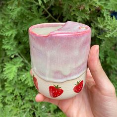 a hand holding a cup with strawberries painted on the outside and inside, in front of green foliage