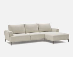 a white sectional couch with pillows on it's back and arm rests in front of an off - white background