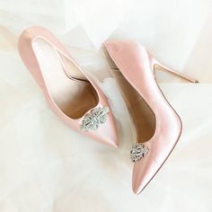 a pair of pink high heeled shoes with a crystal brooch