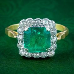 A striking vintage cluster ring built around a natural step cut emerald at its heart, weighing approx. 3.65 carats. It has an intense, vivid green hue and is bordered by sixteen twinkling old mine cut diamonds with SI1 clarity - I colour (approx. 0.80ct total).  Emerald is the birthstone of May. The Romans considered it to be the sacred stone of the goddess Venus and was said to preserve love and provide hope. Its natural green colouring also makes it a stone of springtime and is associated with Vintage Green Emerald Ring Gia Certified, Heirloom Green Cluster Ring, Classic Green Cluster Emerald Ring, Emerald Cluster Ring With Diamonds, Green Emerald Cluster Ring With Diamonds, Green Emerald Cluster Ring With Center Stone, Heirloom Green Diamond Cluster Ring, Heirloom Style Green Diamond Cluster Ring, Vintage Green Jewelry With Halo Setting