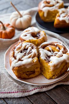 pumpkin cinnamon rolls with icing on a plate next to mini pumpkins and a napkin