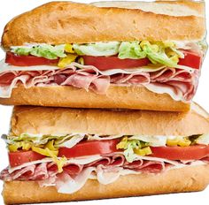 two sub sandwiches with meat, lettuce and tomato on them are stacked high