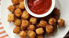 a white plate topped with tater tots next to a bowl of tomato sauce