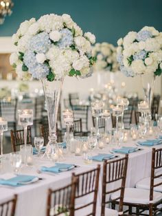 the tables are set up with white and blue flowers in tall vases on them