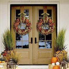 two wreaths on the front door of a house with pumpkins and grass around them