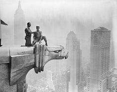 two men sitting on top of a large metal object in the middle of a city