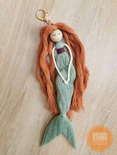 an orange and green mermaid doll hanging from a keychain on a wooden floor