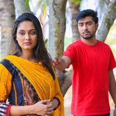 a man standing next to a woman in a yellow sari and red t - shirt