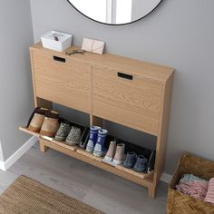 a wooden cabinet with shoes on it in front of a round mirror and rugs