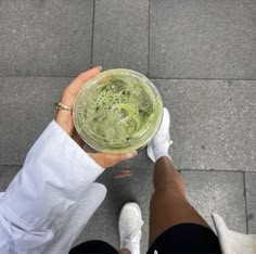 a person holding a cup with green liquid in it on the ground next to their feet