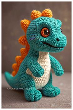 a small crocheted blue and orange dragon sitting on top of a gray surface