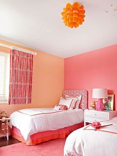 two beds in a room with pink walls and orange curtains