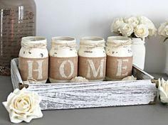 four jars with the word home are sitting on a table next to flowers and vases