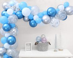 blue and silver balloons are hanging from the ceiling in front of a white table with decorations