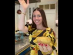 a woman in a yellow and black dress is waving at the camera with her hand up