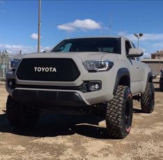 the front end of a white toyota pickup truck parked in a dirt lot with other trucks behind it