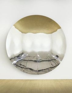 a round mirror hanging on the wall in front of a white wall with gold trim