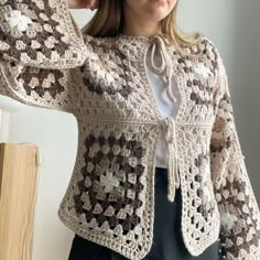 a woman is wearing a crocheted jacket and holding her hands up to her head