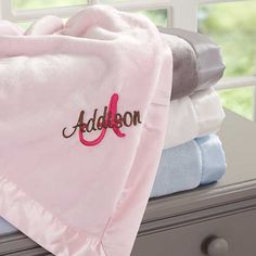 a stack of folded towels sitting on top of a dresser next to a window with the word addon embroidered on it