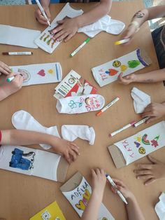 several children are sitting at a table with their hands on paper and crayons