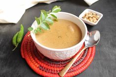 a white bowl filled with soup sitting on top of a red place mat next to a spoon