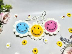 two crocheted smiley face keychains with daisies and flowers in the background