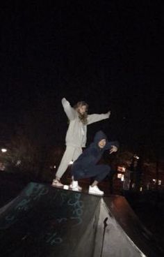 two young people are skateboarding on the edge of a half pipe at night time