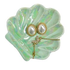 a pair of earrings with pearls on a green leaf shaped dish, set against a white background