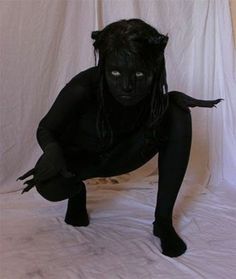 a woman with black makeup and cat ears on her head crouches down in front of a white backdrop