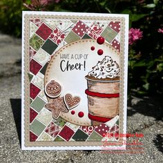 a close up of a card with a cup of cheer on it and flowers in the background