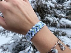 a woman's hand wearing a bracelet with beads and charms on it in front of snow covered trees