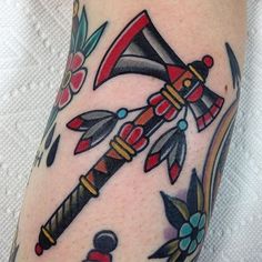 an artistic tattoo on the leg of a woman's leg with flowers and two axes