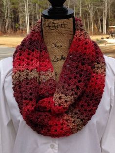 a woman wearing a red and brown crocheted scarf on top of a mannequin