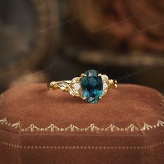 a blue stone ring sitting on top of a brown velvet cushioned box with gold trimmings