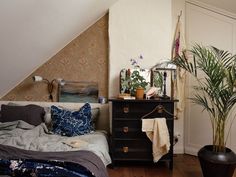 a bedroom with a bed, dresser and potted plant in the corner on top of it