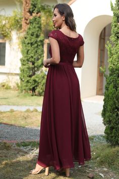 a woman in a long red dress standing on the grass with her back to the camera