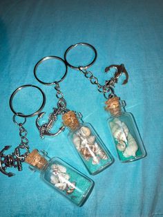 three glass bottles filled with sand and sea shells on a blue cloth covered tablecloth