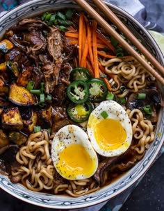 a bowl filled with noodles, eggs and vegetables next to chopsticks on a table