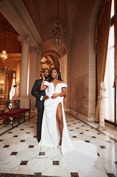 a man and woman in formal wear posing for a photo inside an ornate building with chandeliers