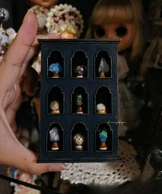 a hand holding a small black box filled with miniature rings and knick - knacks