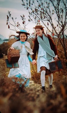 two people dressed in historical clothing walking through a field holding baskets and suitcases on their backs