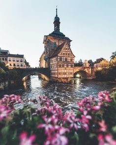 an old building on the side of a river with flowers growing in front of it