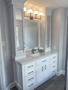 a white bathroom vanity with two sinks and large mirrors on the wall above it, along with three lights