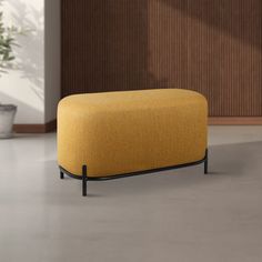 a yellow ottoman sitting on top of a white floor next to a potted plant