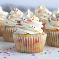 several cupcakes with white frosting and sprinkles on a plate