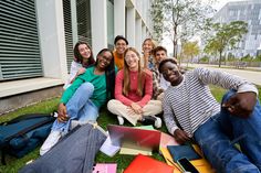 a group of young people sitting on the grass with laptops in front of them