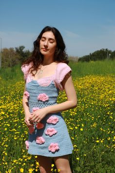 a woman standing in a field full of flowers wearing a dress with crochet